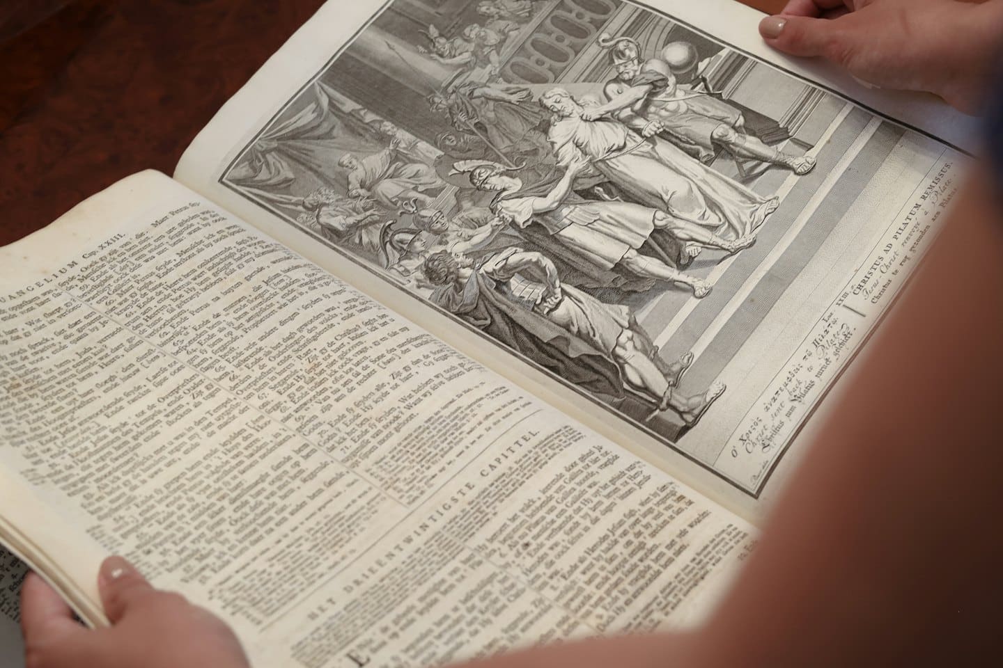 Hände halten ein altes Buch mit Text und Gravuren offen.