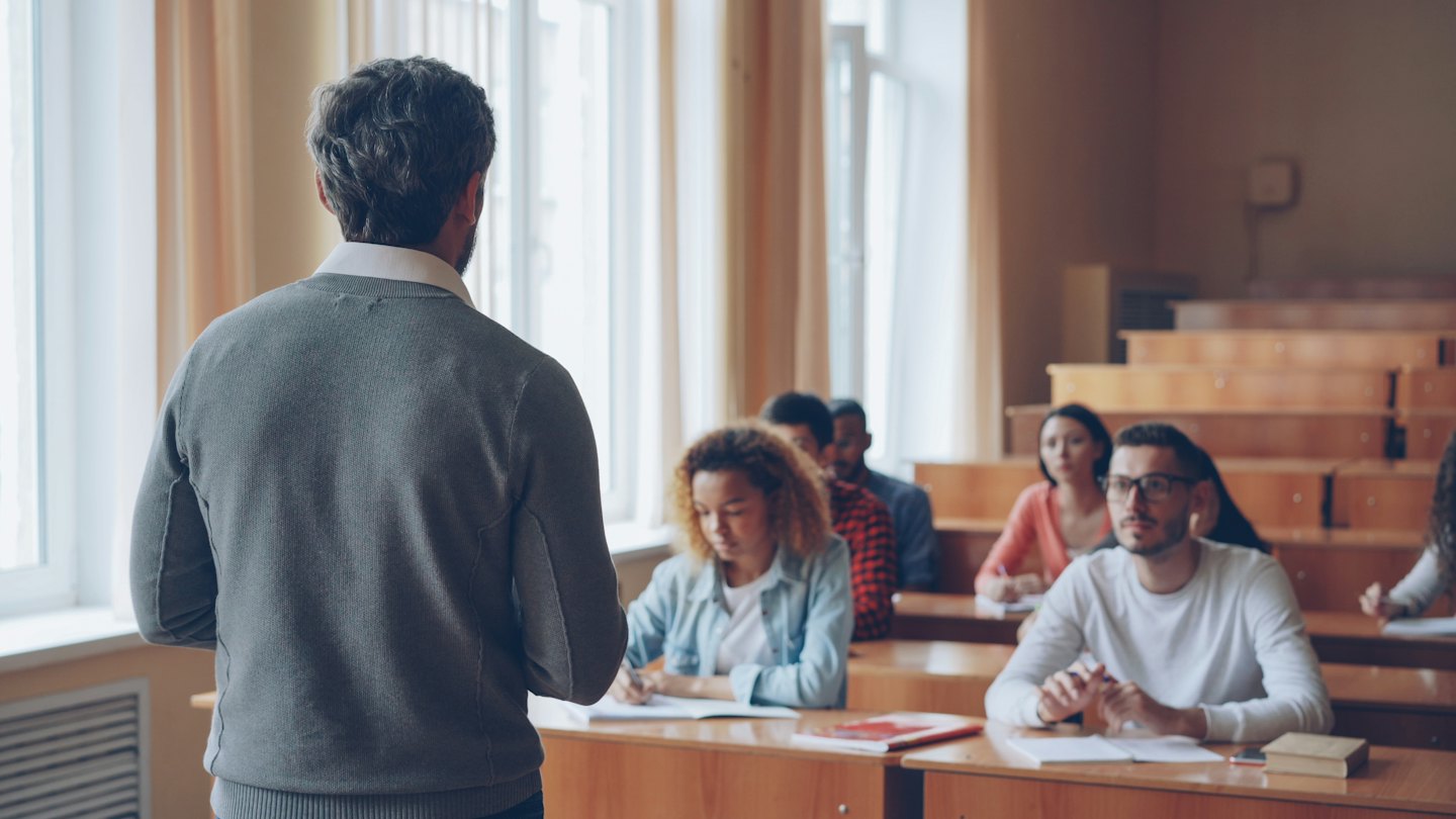 Lehrerin unterrichtet diverse Schüler in einem sonnendurchfluteten Hörsaal.